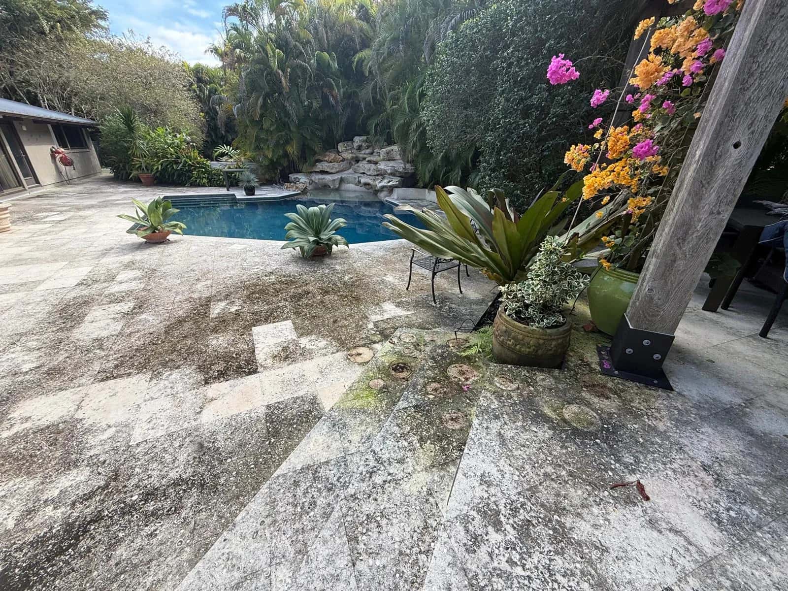 Dirty travertine deck beside a rock waterfall pool before cleaning